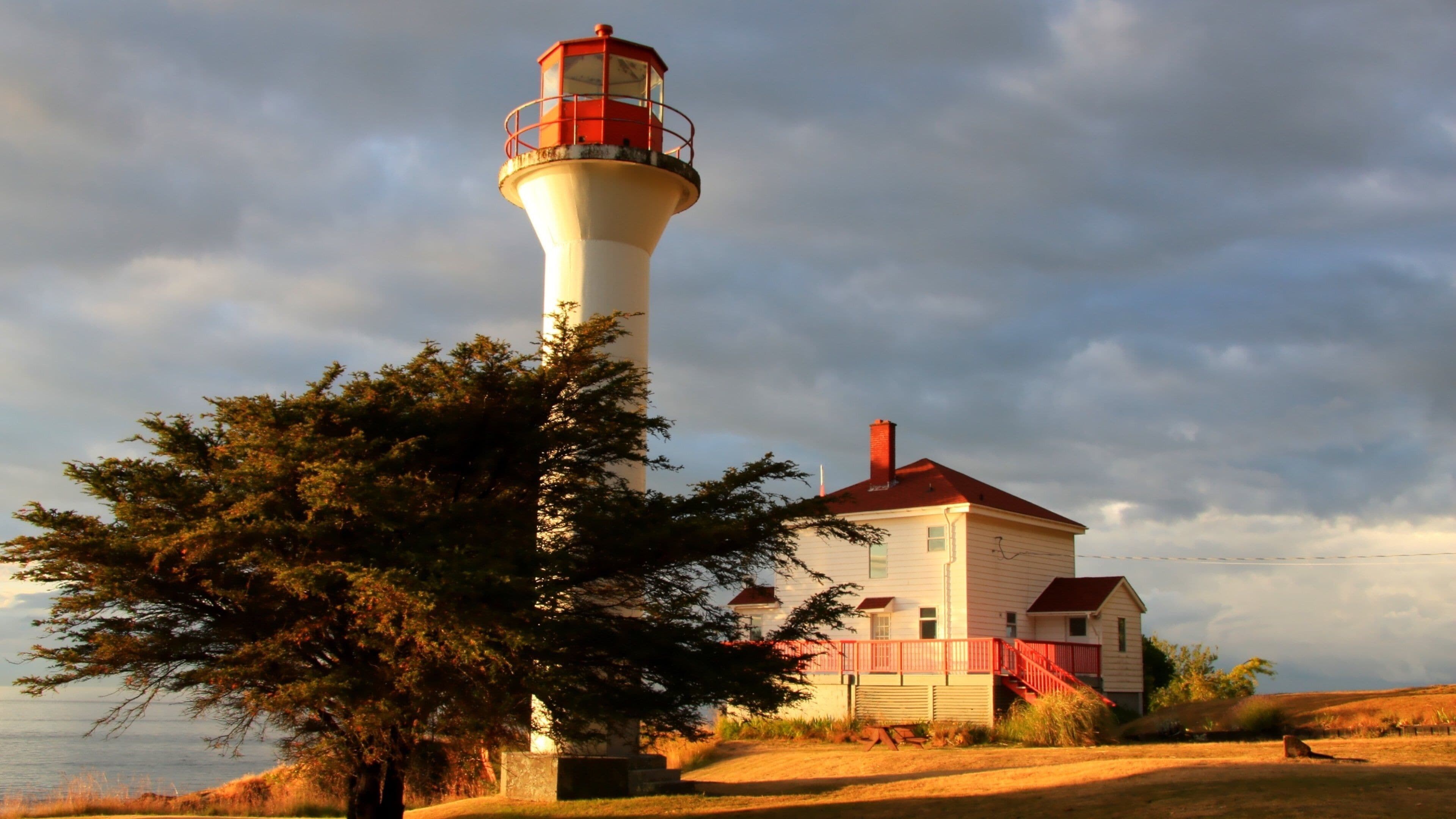 A lighthouse with a red top, a white base, and a red-roofed house nearby.
