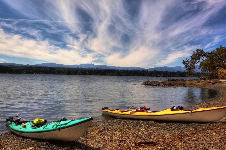 Two kayaks on a pebbly shore with a lake and mountains in the background.