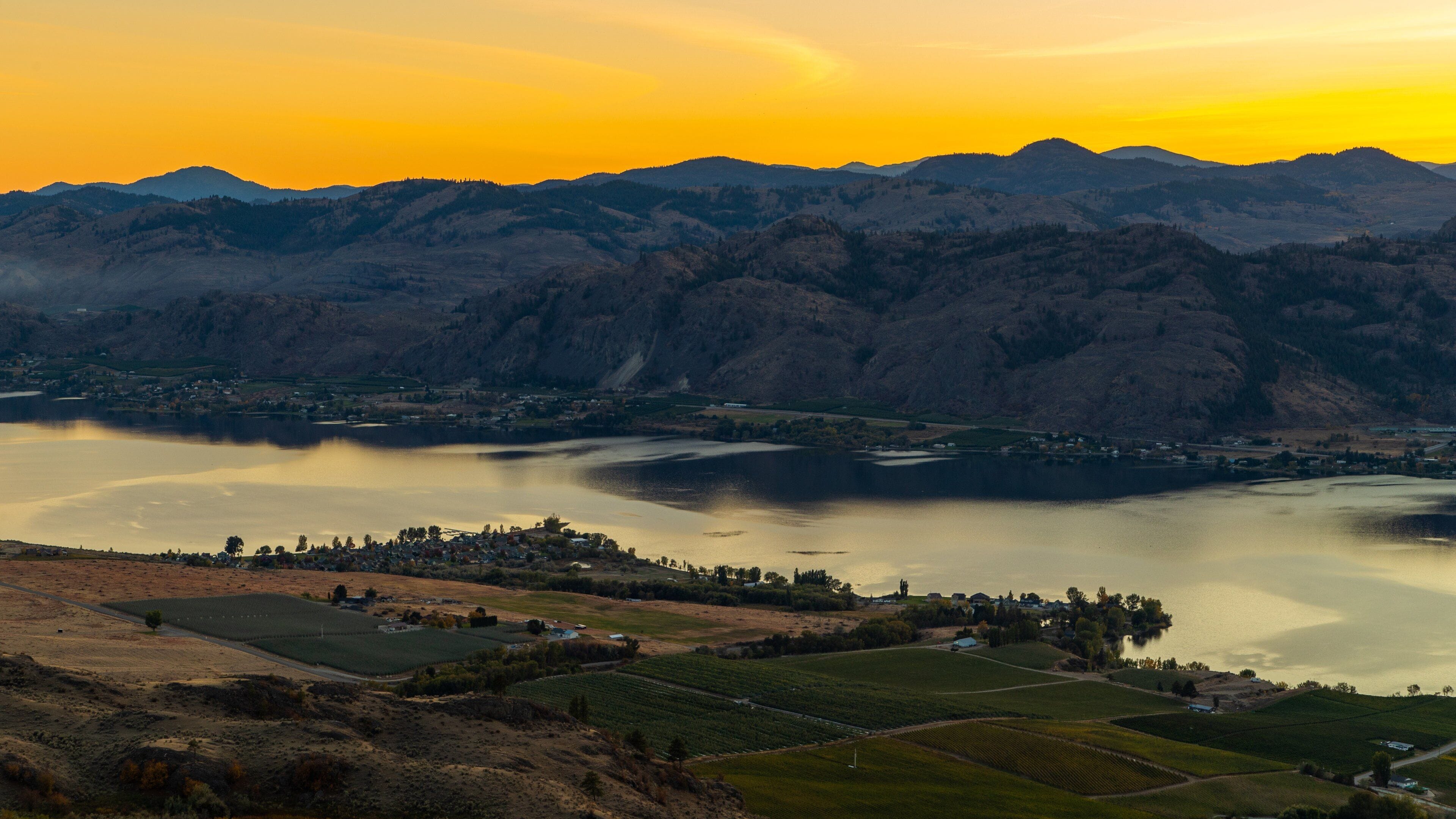 A mountainous landscape with a lake and a small town at sunset.