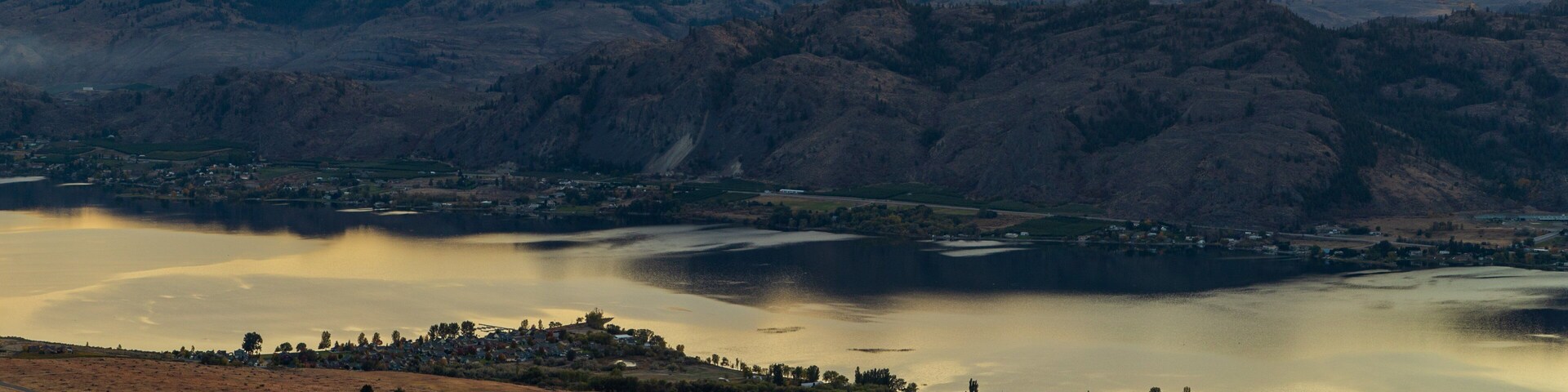 Un paisaje montañoso con un lago y un pequeño pueblo al atardecer.