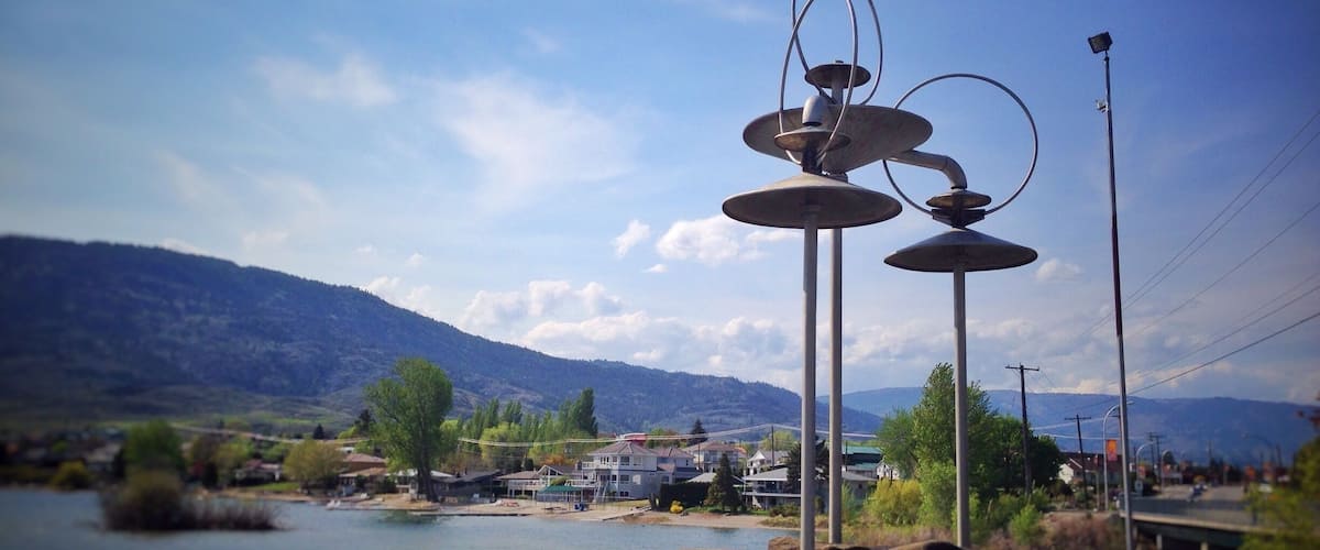 A lake with mountains in the background, a bridge, and a metal sculpture in the foreground.