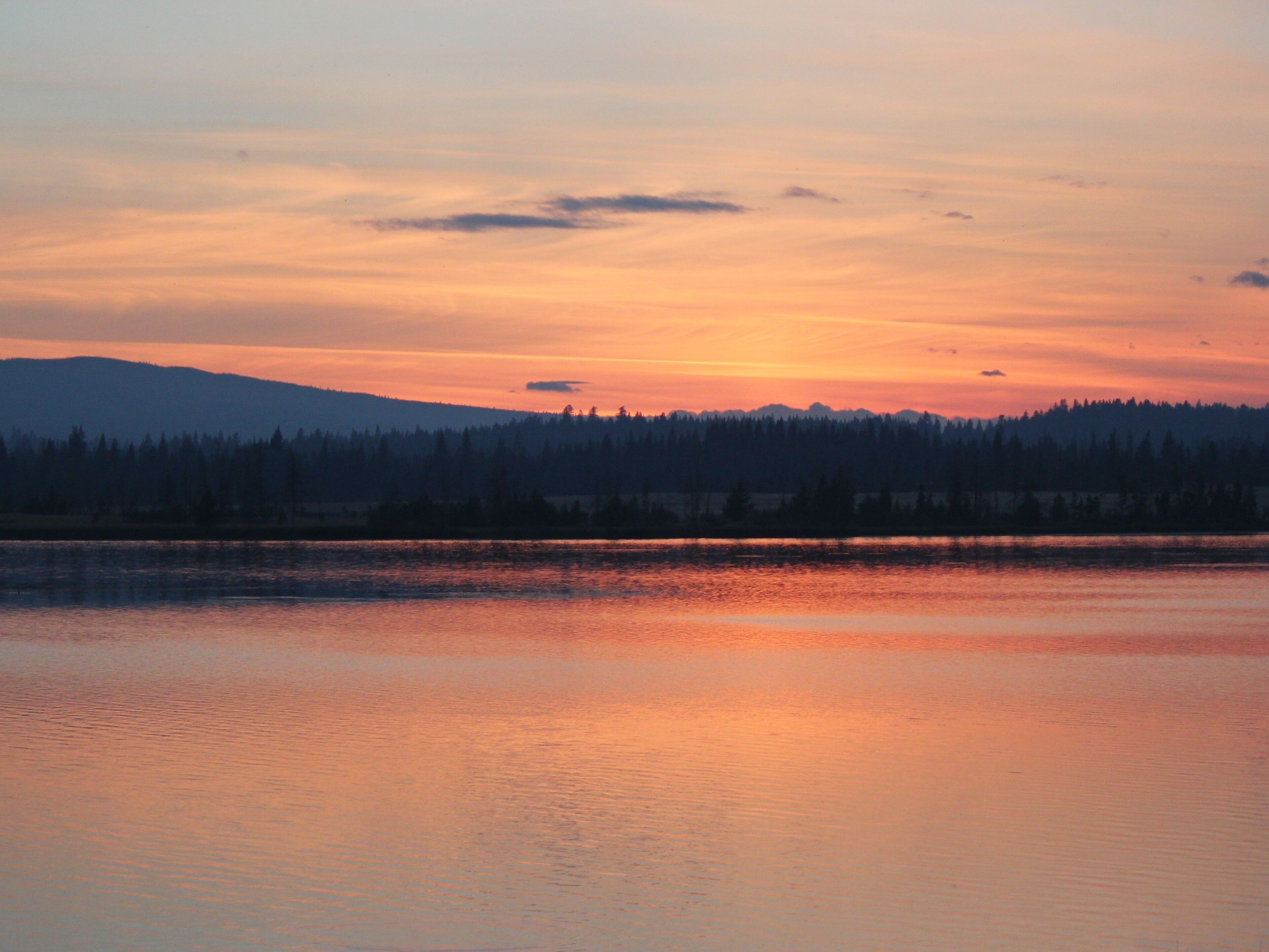 A sunset over a calm lake with a forested mountain in the background.