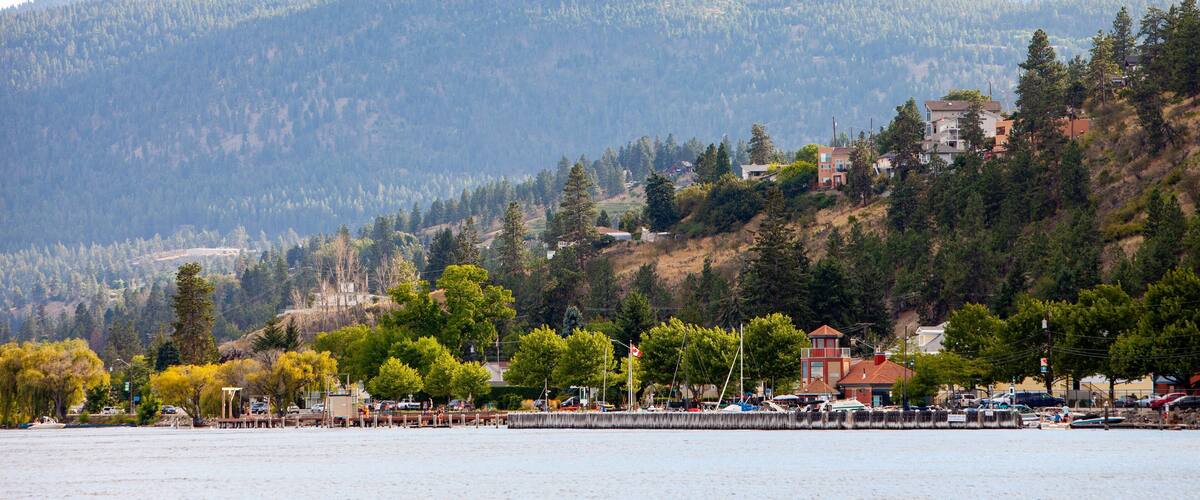 A lakeside town with houses on a hillside, surrounded by mountains and trees.