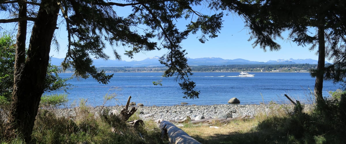 A rocky shoreline with a boat on the water and mountains in the background.