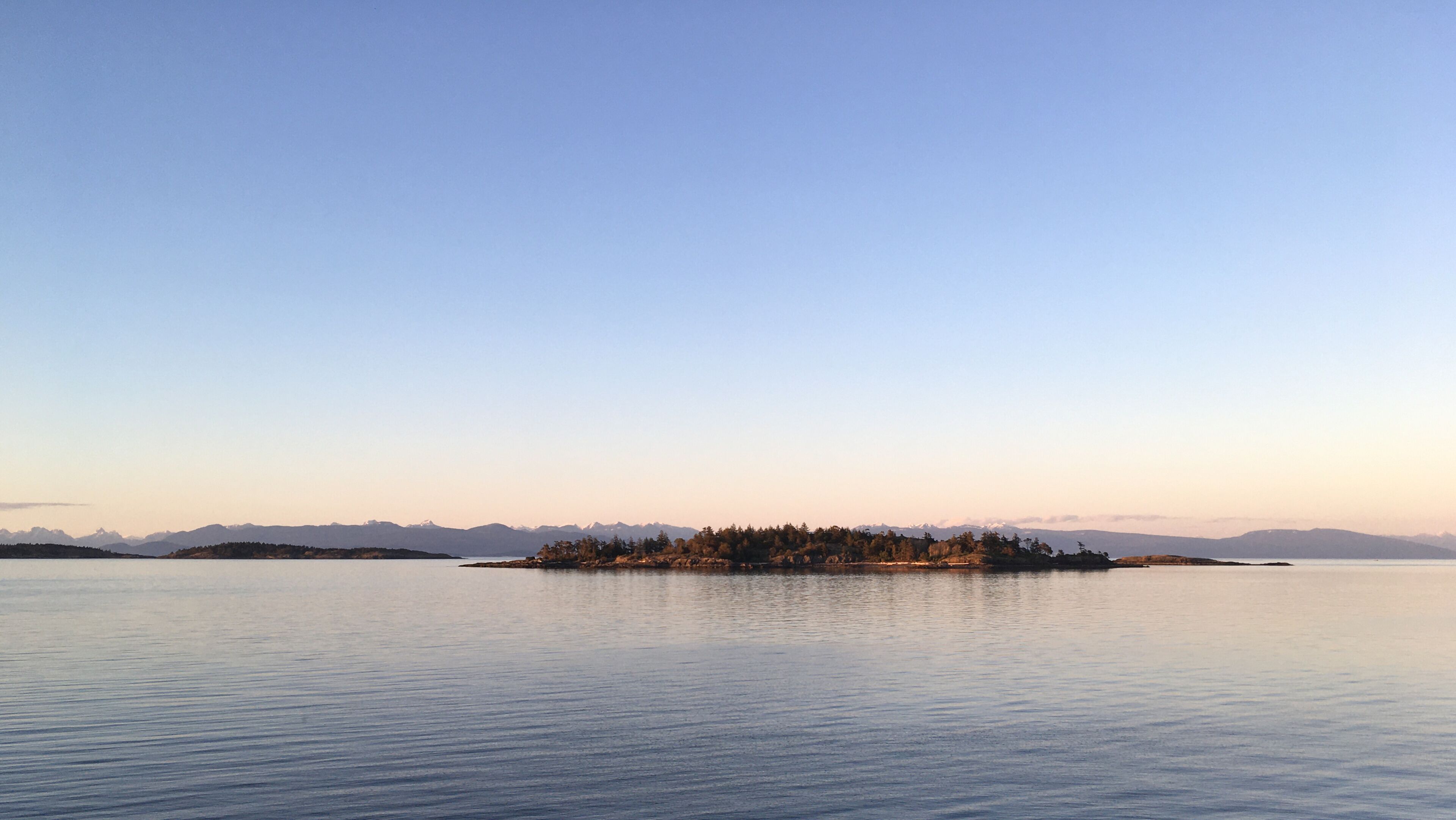 Un lago tranquilo con una pequeña isla en el centro, rodeado de montañas a lo lejos.