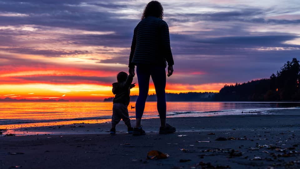 A sunset over a beach with silhouettes of a woman and child.