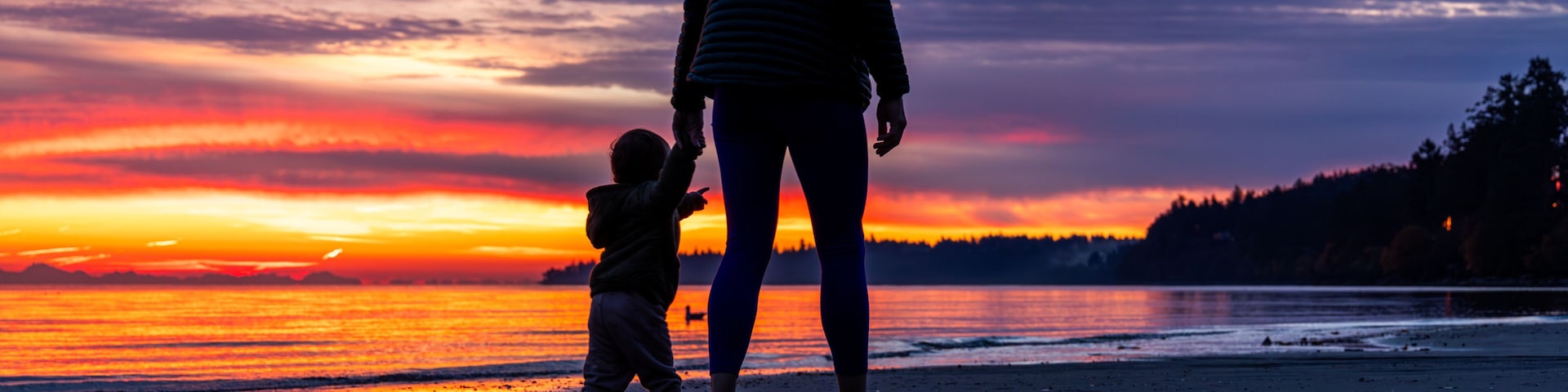 Um pôr do sol sobre a praia, com silhuetas de uma mulher e uma criança.