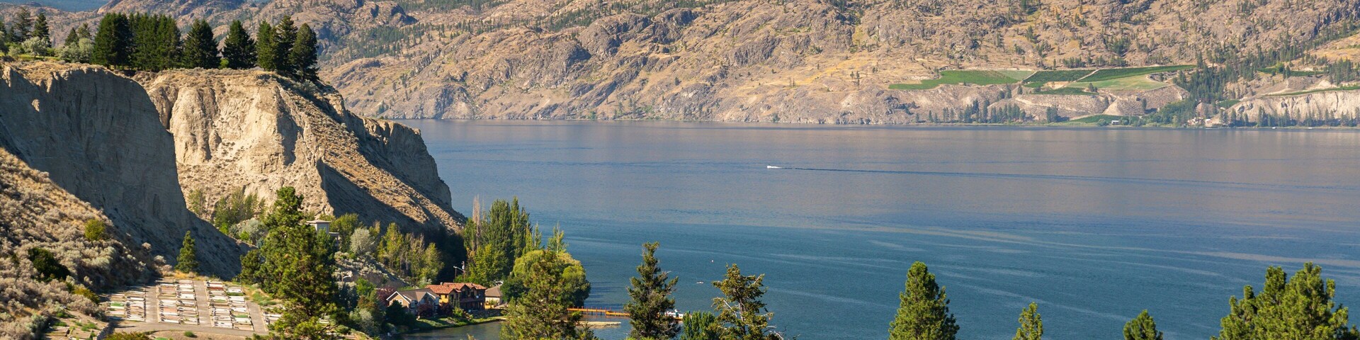 Un paisaje montañoso con un lago, un acantilado rocoso y un pequeño poblado con casas y una carretera.