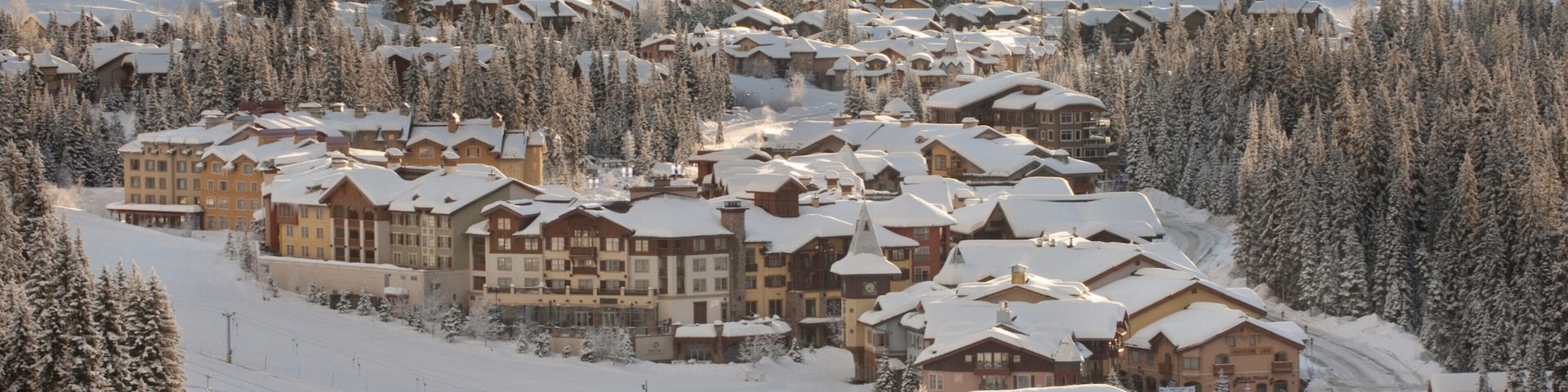 Estância de esqui coberta de neve, com edifícios de chalés e teleféricos.