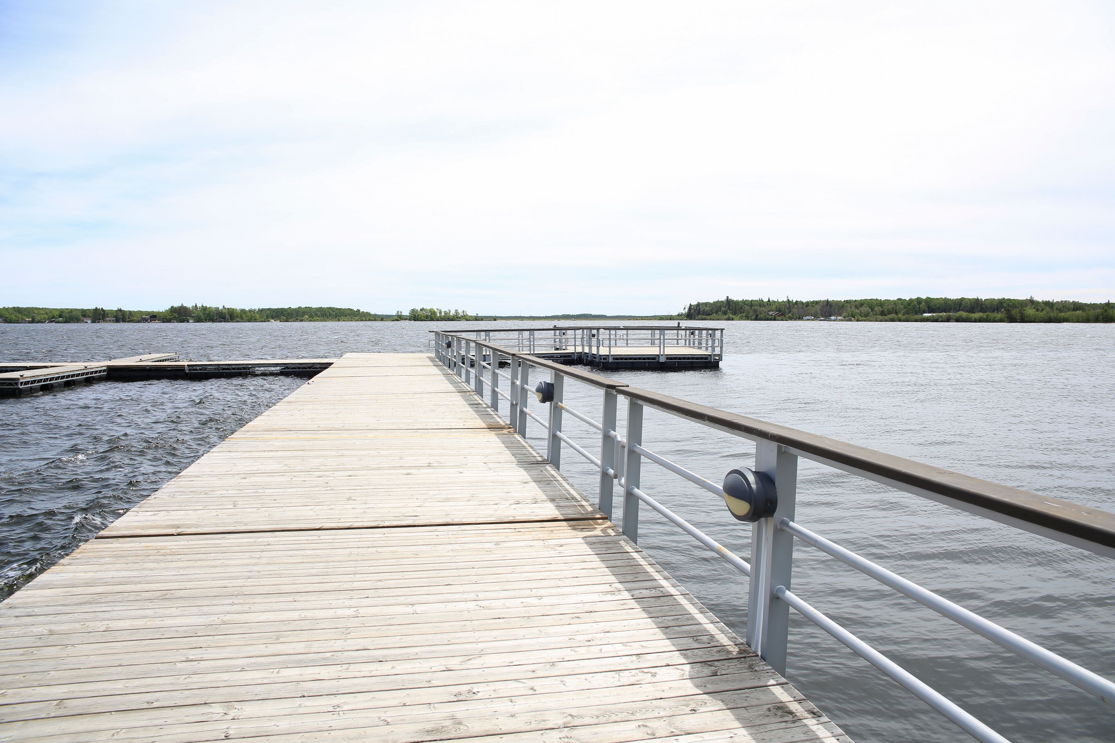 A wooden pier extending into calm water with a metal railing.