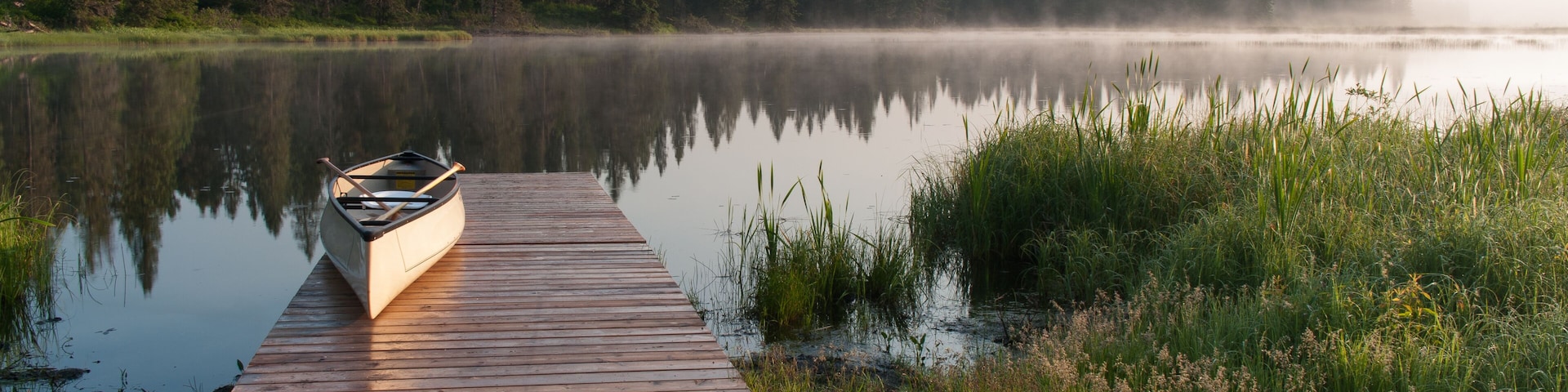Canoe on a dock at a lake during a misty sunrise.