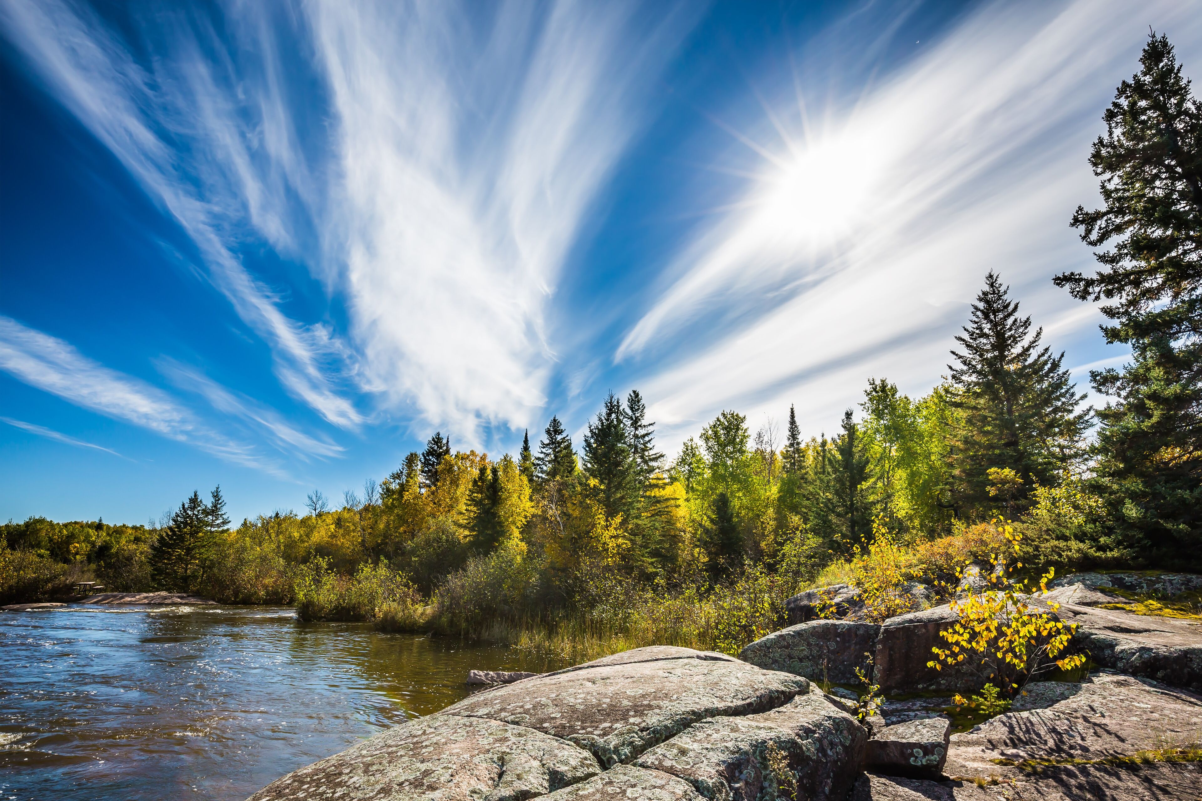 A river, rocky terrain, and a forest with autumn-colored trees.