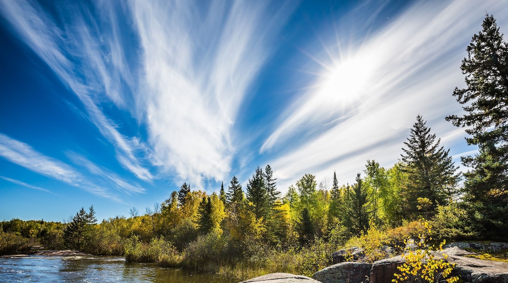 A river, rocky terrain, and a forest with autumn-colored trees.