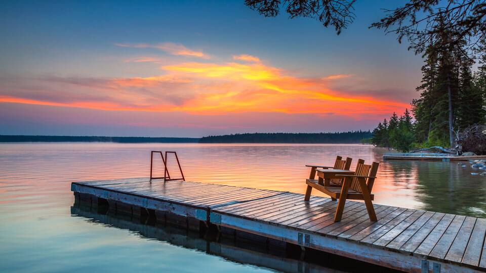 A wooden dock extending into calm water with a sunset in the background.