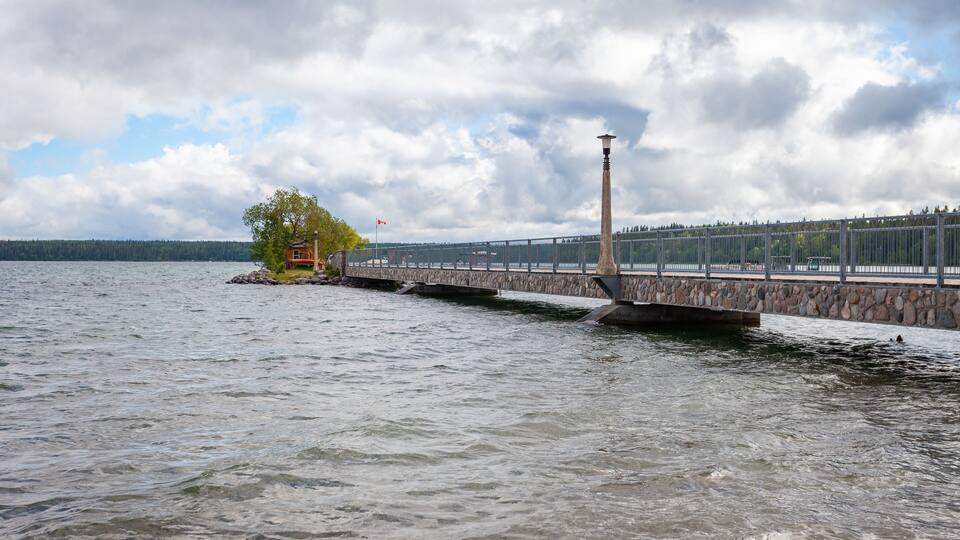 A stone pier extending into a lake, a wooden structure on the shore, and a distant forested shoreline.