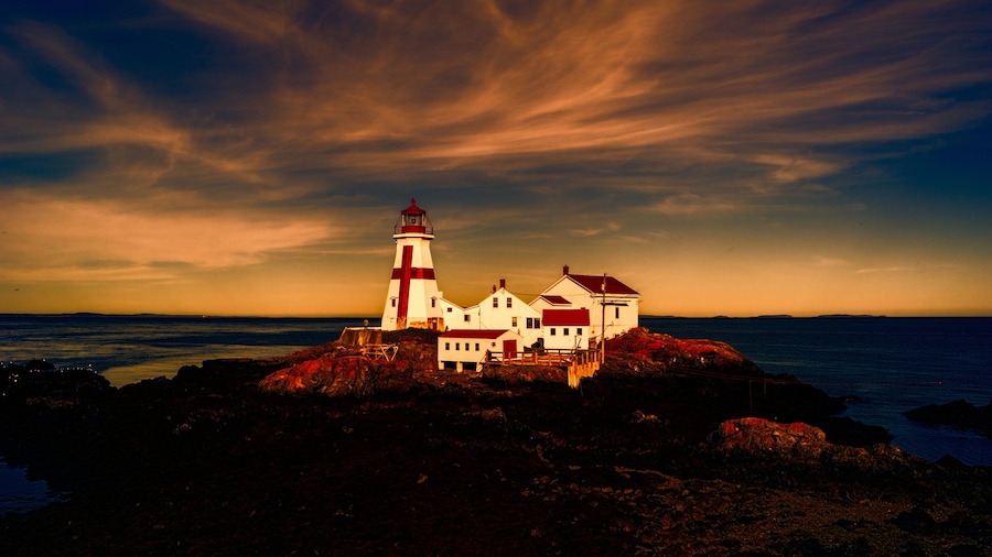 Un phare et des bâtiments blancs sur une côte rocheuse, avec l’océan en arrière-plan.