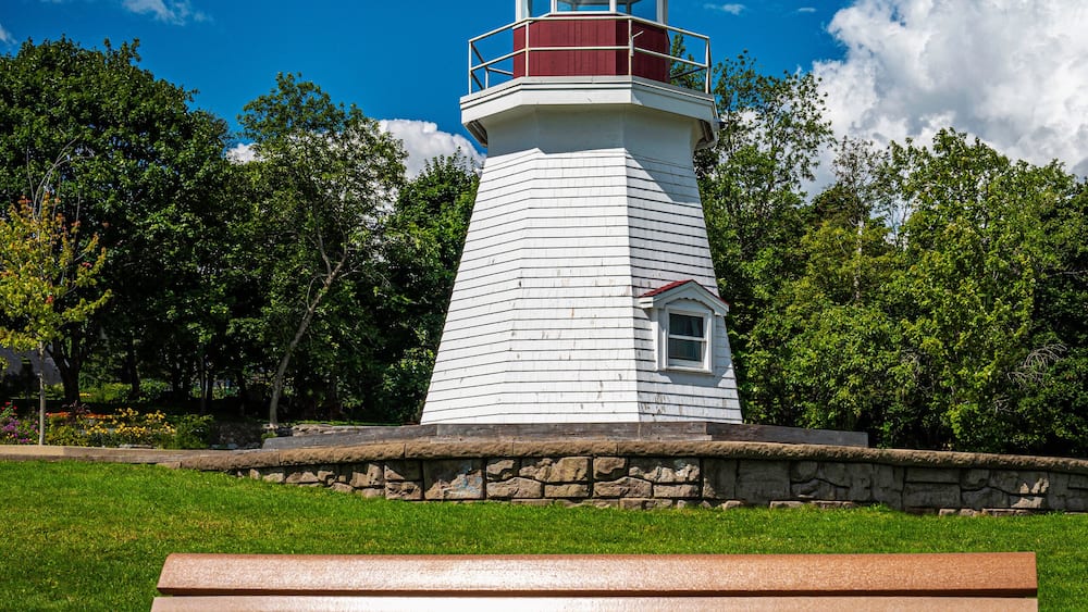 Renforth Lighthouse on the riverbank of Kennebecasis River in Rothesay, New Brunswick, Canada. Empty resting bench and tranquil cloudscape over summer green forest and hilly community park.