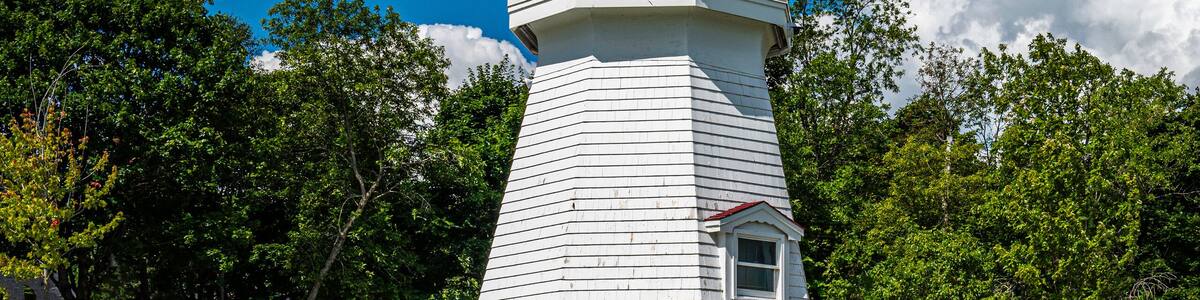 Renforth Lighthouse on the riverbank of Kennebecasis River in Rothesay, New Brunswick, Canada. Empty resting bench and tranquil cloudscape over summer green forest and hilly community park.