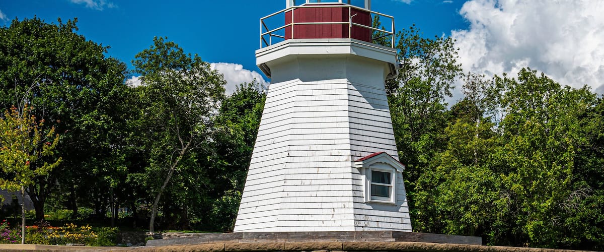 Renforth Lighthouse on the riverbank of Kennebecasis River in Rothesay, New Brunswick, Canada. Empty resting bench and tranquil cloudscape over summer green forest and hilly community park.