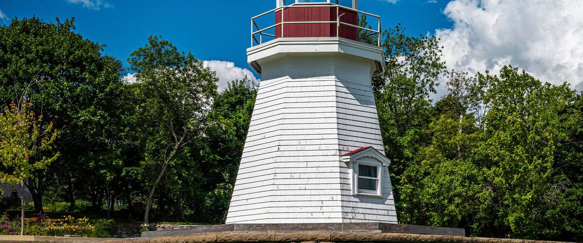 A white lighthouse with a red top, a wooden bench in the foreground, and a stone wall behind it.