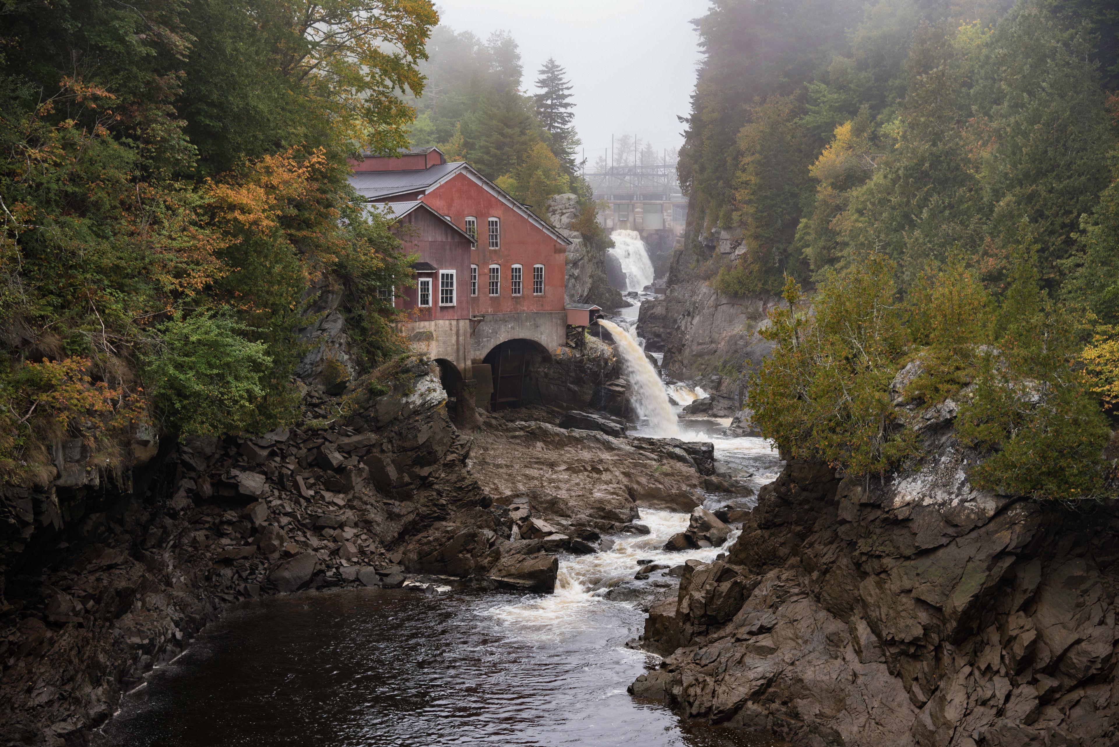 A red building with a waterfall in a forested valley.