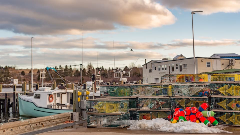 A harbor with a boat docked, fishing cages, and a building in the background.