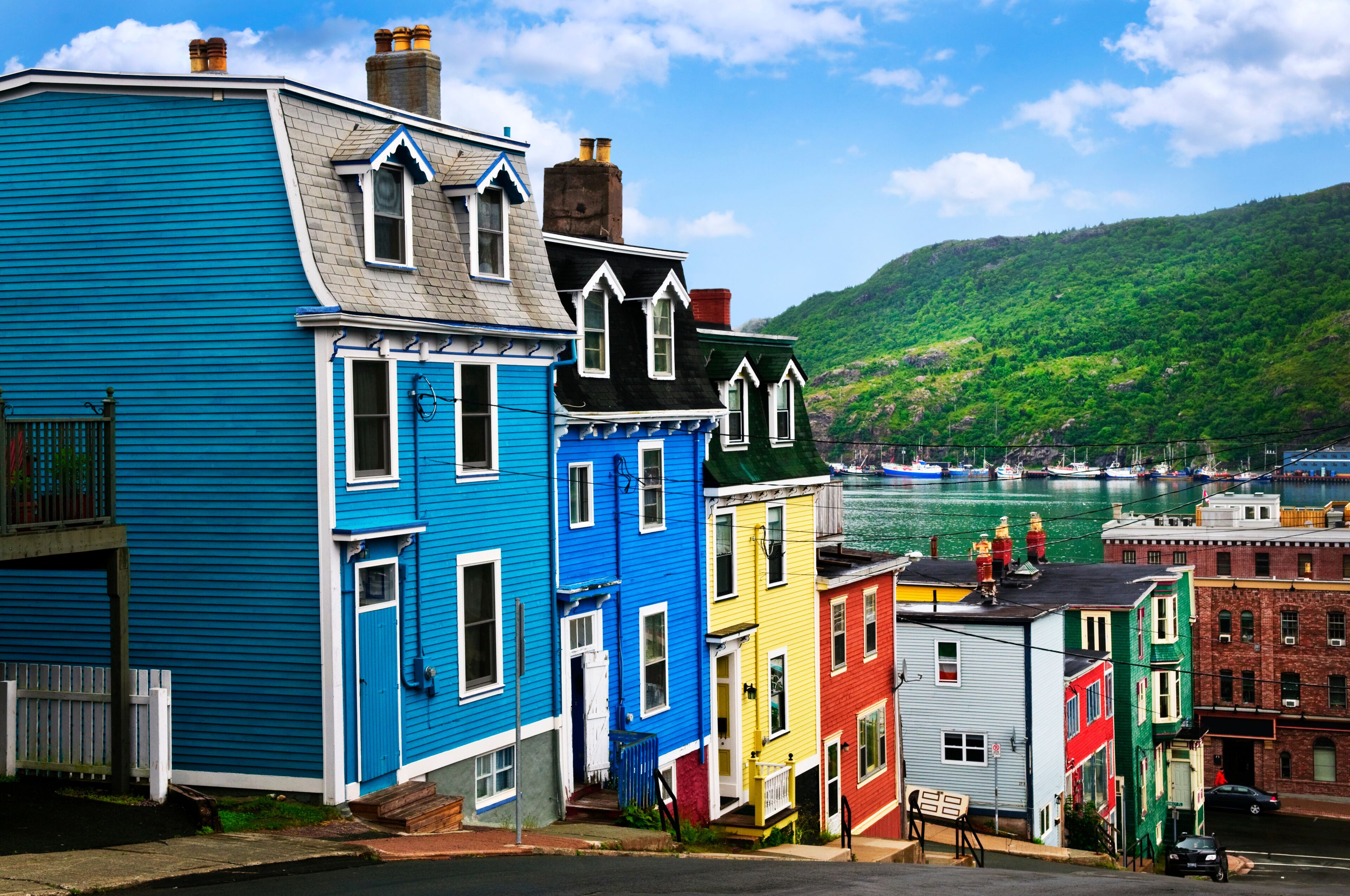 A row of colorful houses by a waterfront with a green hill in the background.