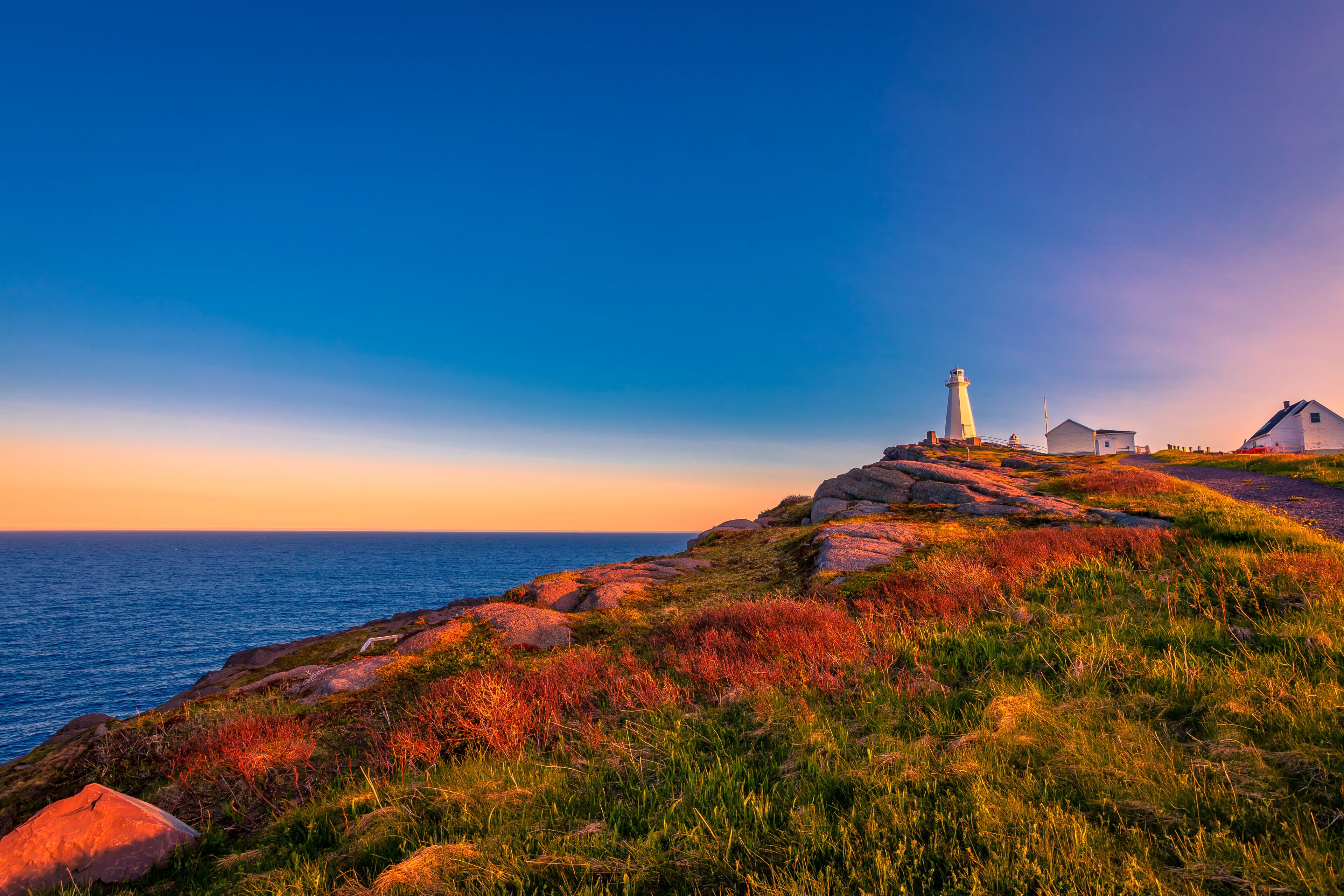 A coastal landscape with a lighthouse, grassy terrain, and a clear sky.
