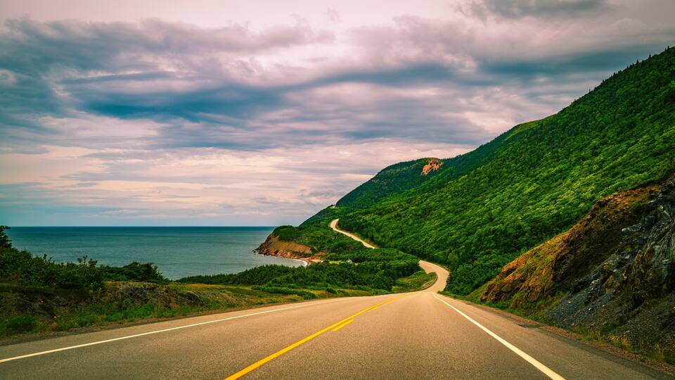 A winding coastal road with lush green hills and a view of the ocean.