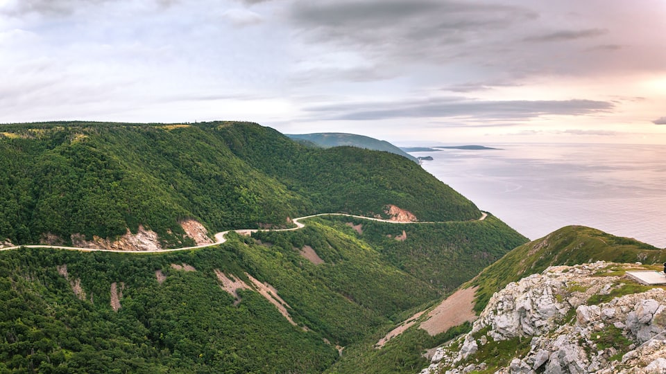 A winding mountain road, lush green hills, and a body of water in the distance.