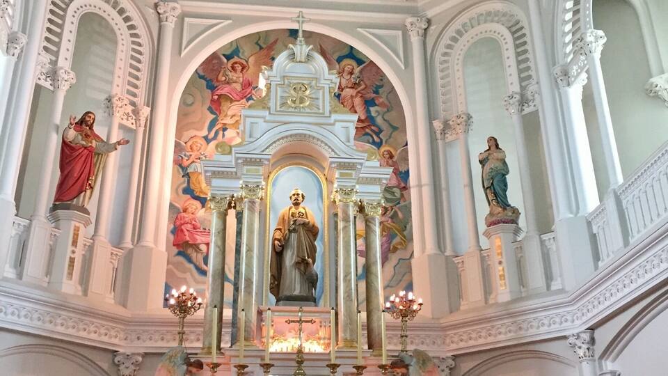 An ornate church interior with a central altar, religious statues, and detailed frescoes on the ceiling.