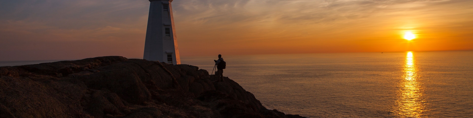 Photographer at Lighthouse at Ocean Sunrise Orange Horizon Blue Skies