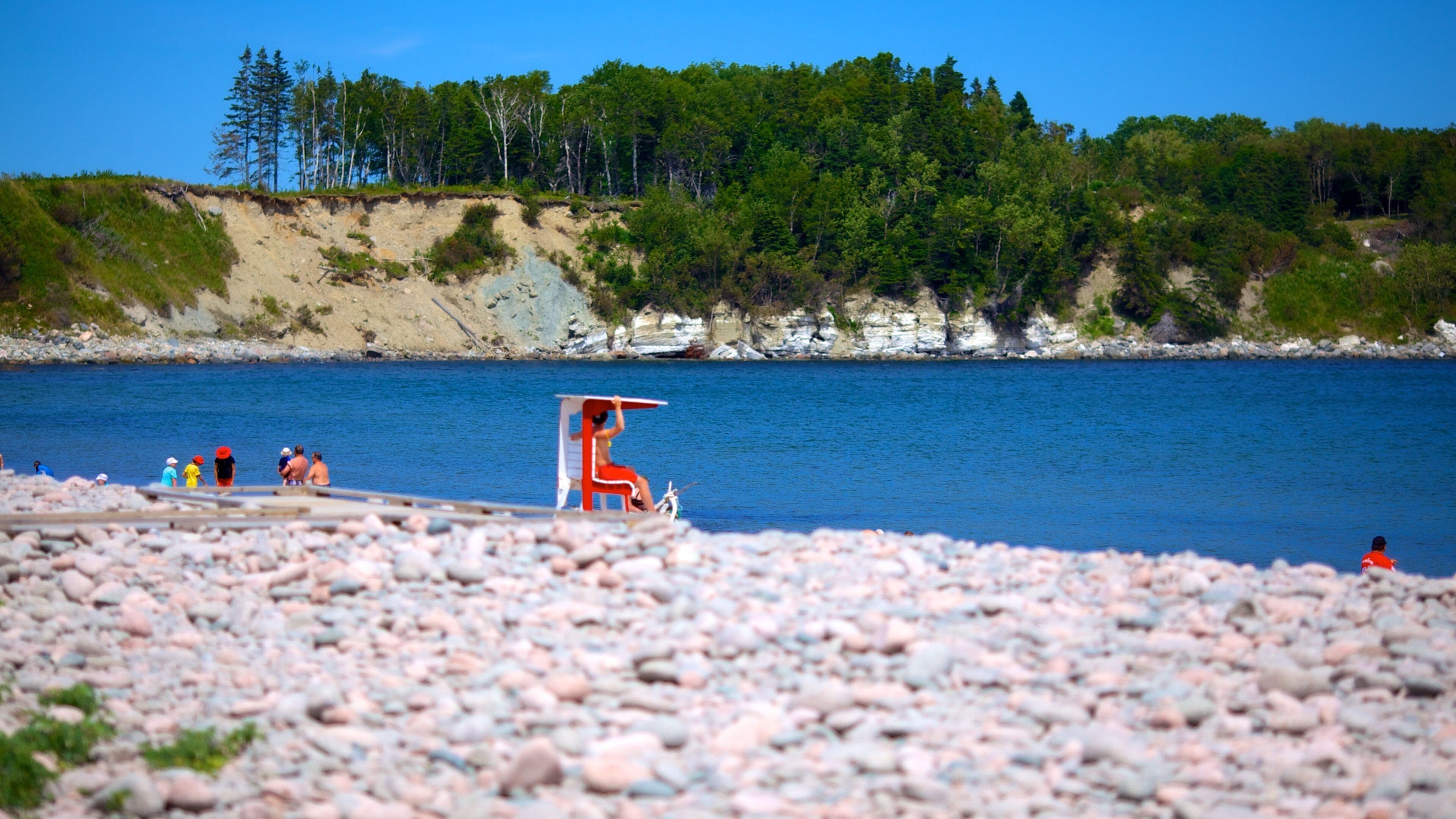 A rocky beach with a lifeguard chair and people in the water.
