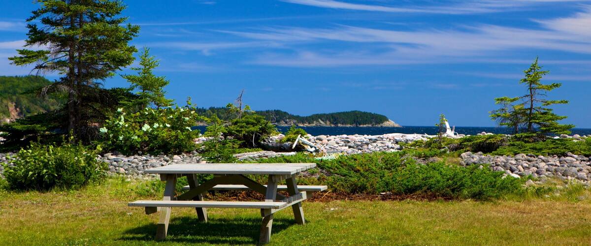 A picnic table by a rocky shoreline with a clear blue sky and distant mountains.