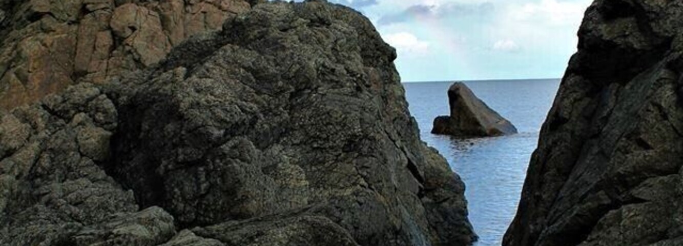 Costa rocosa con un arcoíris sobre una formación rocosa marina.
