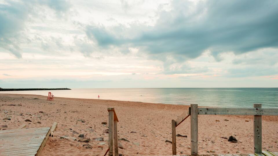 A wooden boardwalk leading to a sandy beach with a lifeguard chair and a rocky shoreline.