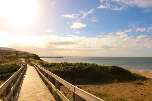 A wooden boardwalk leading to a beach with a clear sky and distant land.