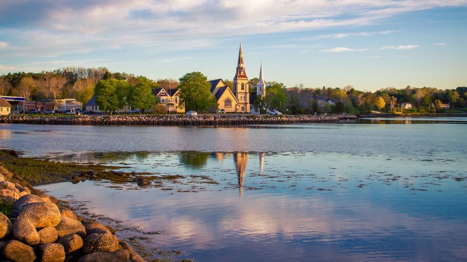 A calm lake with a church and residential buildings in the background.
