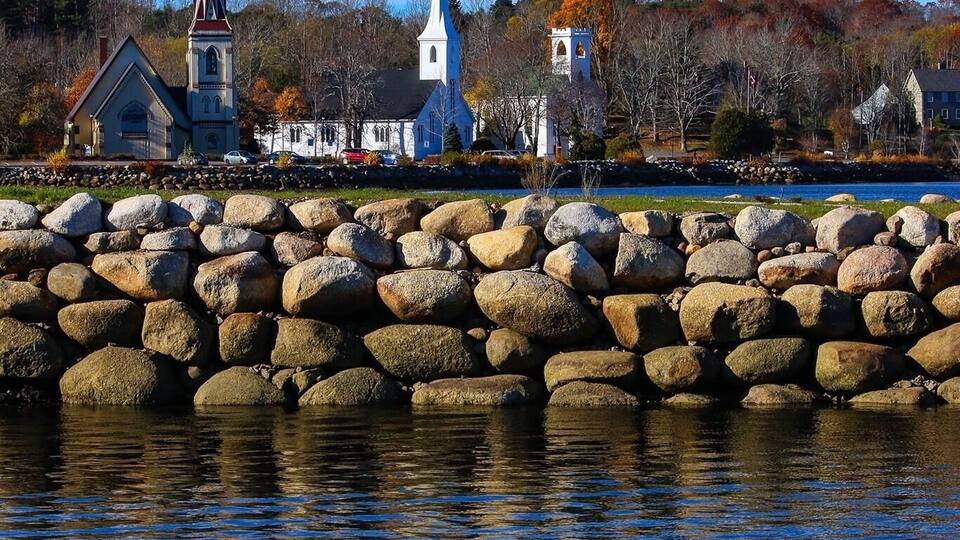 A calm lake with a wooden dock, a small boat, and two church steeples in the background.