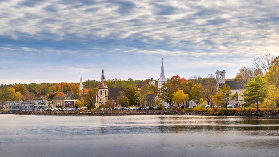 A lakeside town with colorful autumn trees, historic buildings, and a clear sky.