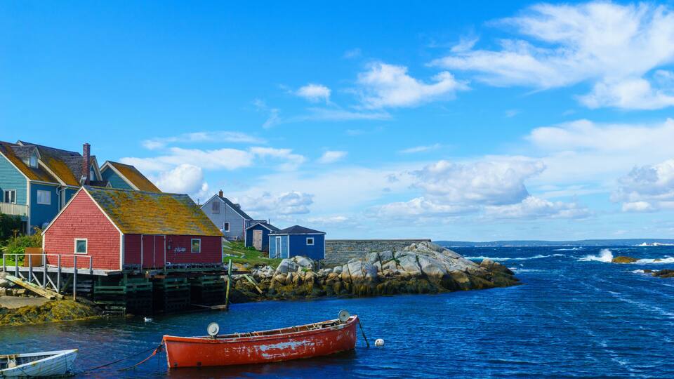 A coastal scene with a red boat, a white boat, and colorful buildings by the water.
