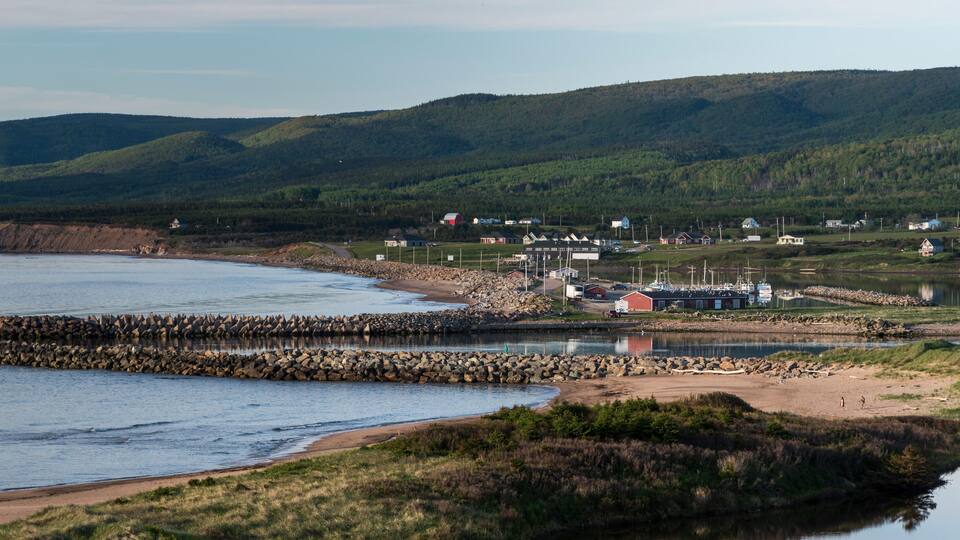 A coastal town with a rocky breakwater, a marina, and houses on the hillside.
