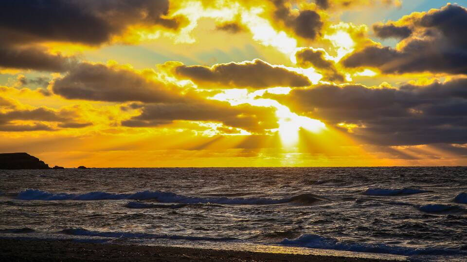 A sunset over the ocean with waves and a silhouette of land in the distance.