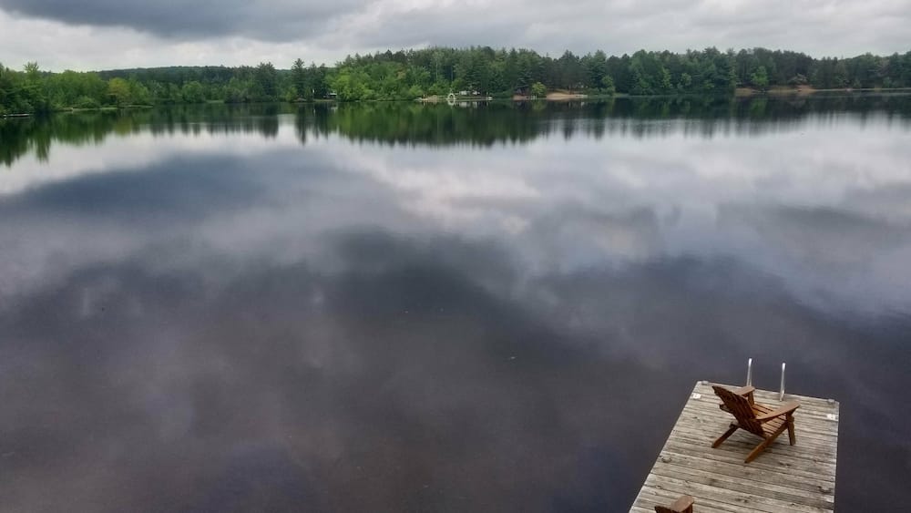 A calm lake with a wooden dock and chairs.
