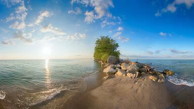 A beach with a rocky shoreline, waves, and a clear sky with clouds.