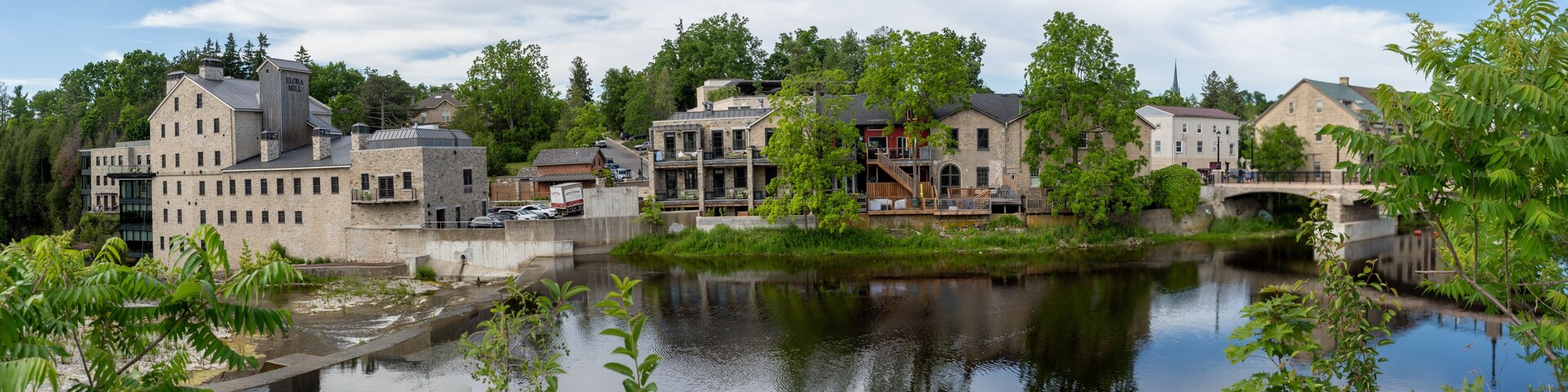 Un pueblo a orillas del río con edificios históricos, un puente y abundante vegetación.