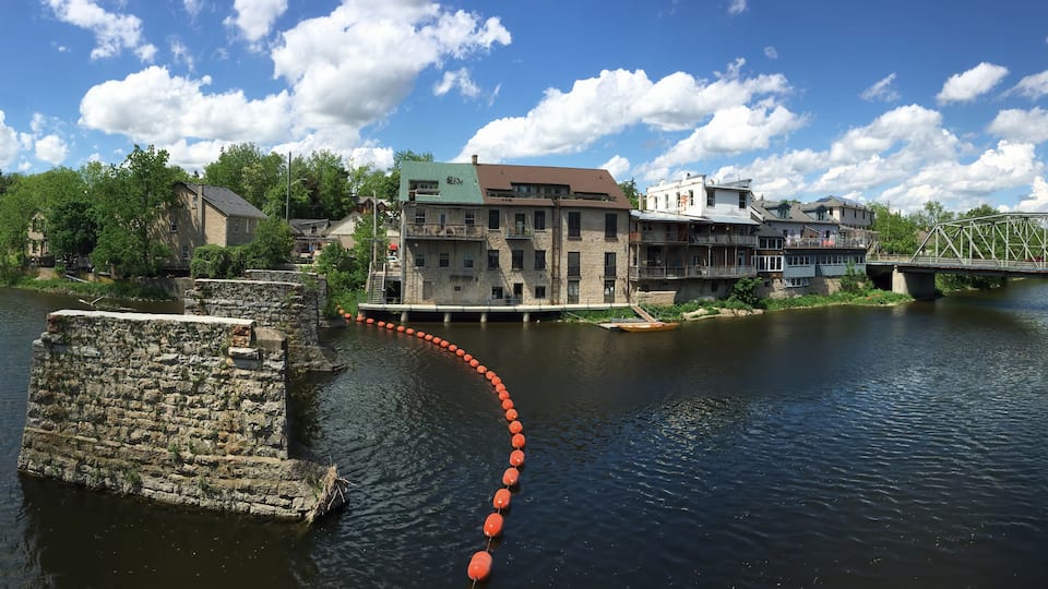 A river with a stone structure, a bridge, and buildings along the banks.