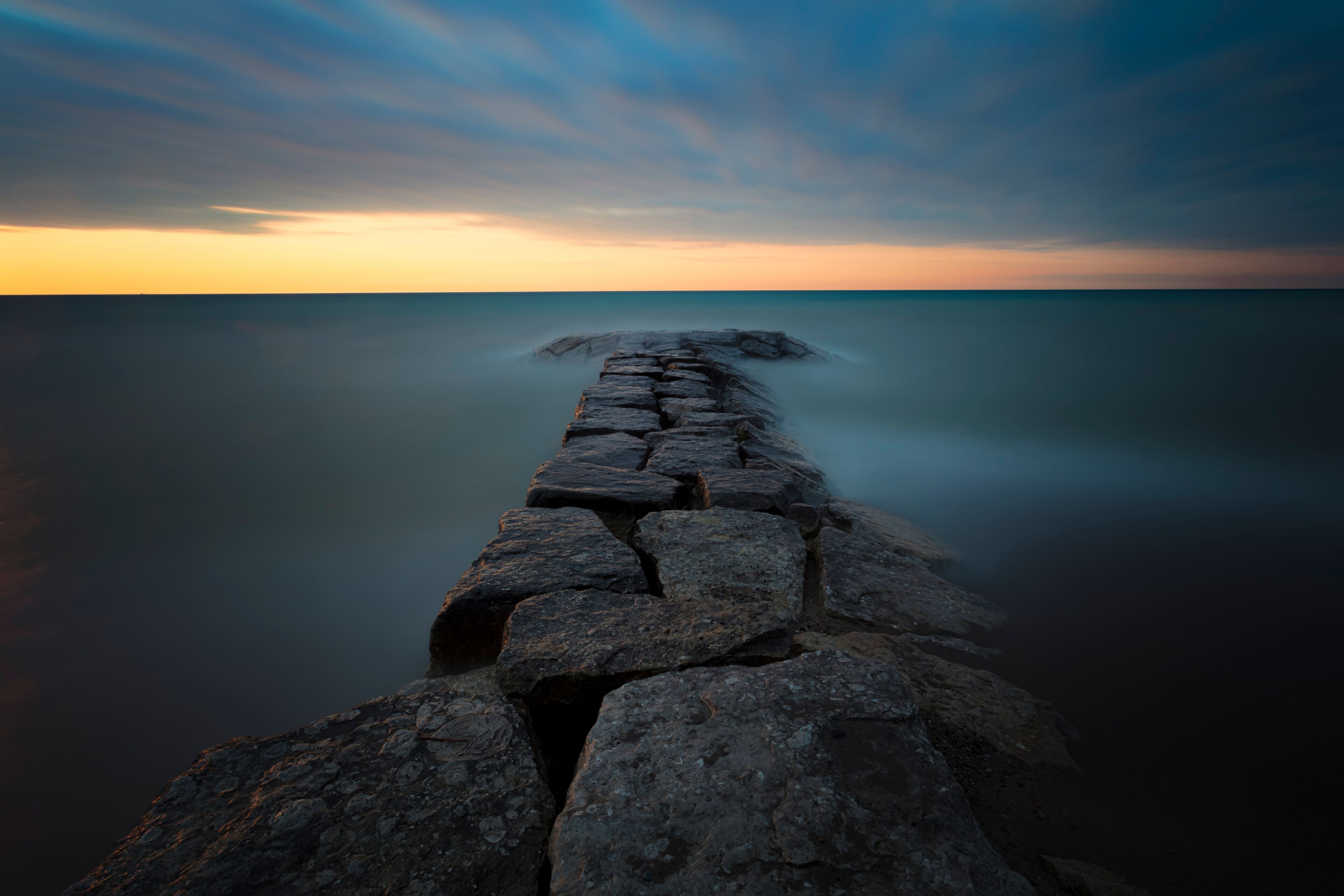 A stone pier extending into calm waters at sunset.