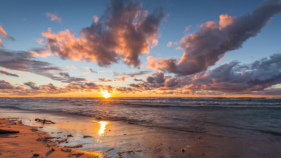 A sunset over a beach with scattered driftwood and waves.