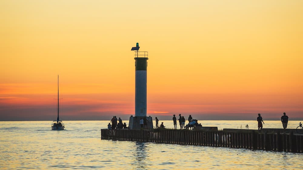Ein Leuchtturm im Abendrot mit Menschen auf einer Mole.